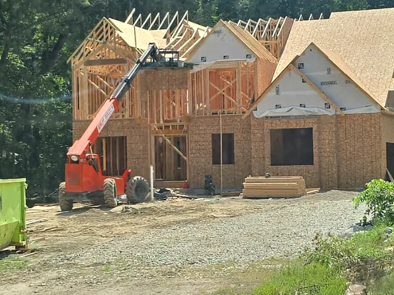 Two story custom home framed with roof trusses set and a telehandler on site, Novi MI