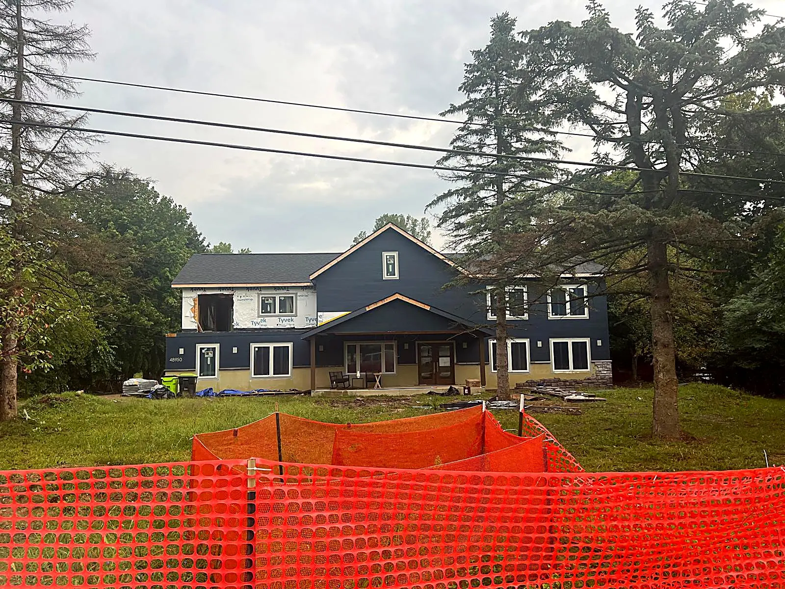 Finished two story home with dark blue siding behind construction fencing, Novi MI